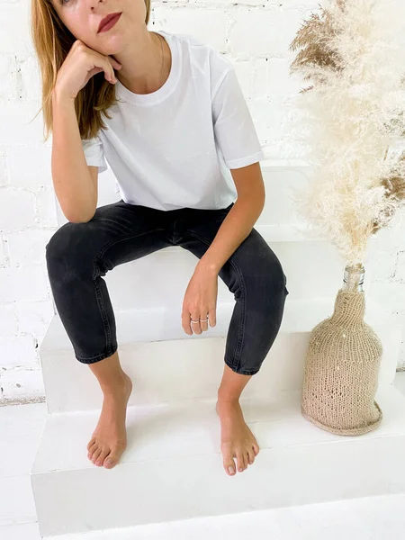 Schöne junge Frau in weißem T-Shirt und schwarzen Jeans sitzt auf der Treppe — Stockfoto