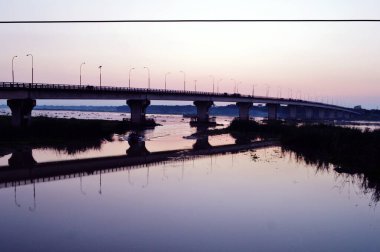 Gün batımında köprünün gölgesinde sokak lambaları suyla kaplı.