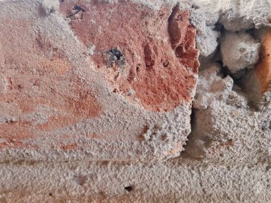 Kırık alçılı, kırmızı tuğlalı ve tozlu, pürüzlü yüzeyi olan yıpranmış bir duvara yakın plan. Projelerde inşaat, yenileme, doku ve endüstriyel temalı görseller için harika.