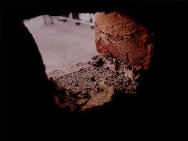 Küçük bir tuğla pencere aralığından yakından bakınca tozlu, sert havan ve aşınmış dokuyu, yaşı, ihmal ve endüstriyel yapı detaylarını ılık toprak tonları ve dramatik gölgelerle anımsatıyor..