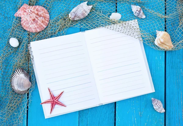 Open notebook on old blue wooden table with fishing net, cockles — Stock Photo, Image