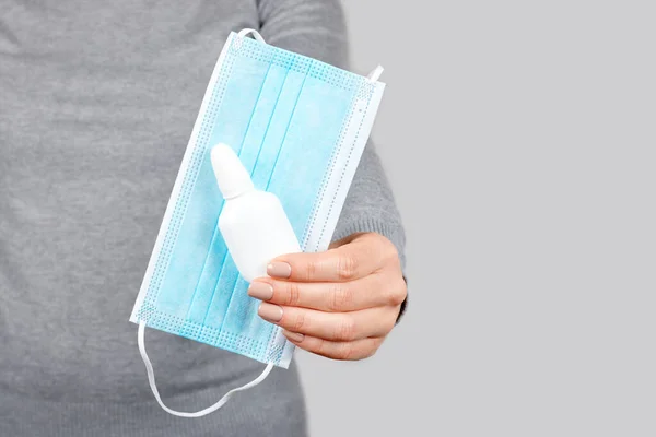 Hand with protective facial mask and nasal spray.