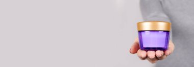 Gri üzerine mor kozmetik kavanozu olan el..