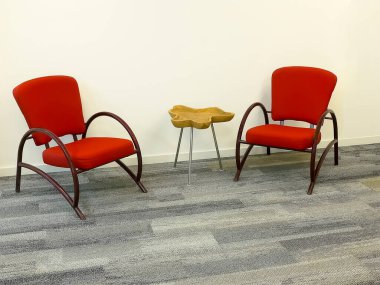 Two red armchairs and a table against the background of the wall.