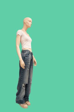 Full-length image of a female display mannequin wearing white short-sleeved blouse and gray ripped jeans isolated on a green background
