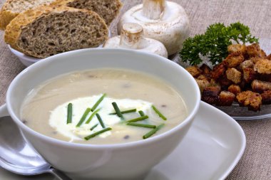 Kremalı ve mantar çorbası yanında soğan ve taze kahverengi ekmek ile süslenmiş.,