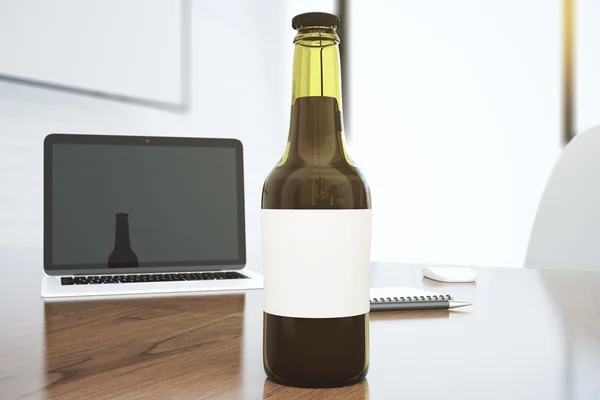 Bürotisch mit Laptop, Glasflasche mit weißem Etikett und — Stockfoto
