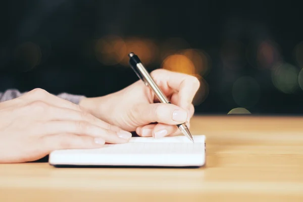 Girl writing in the diary on wooden table at night, close up — Stock Photo, Image