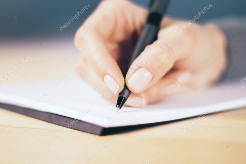 Girl hand with pen and notebook on wooden table, close up