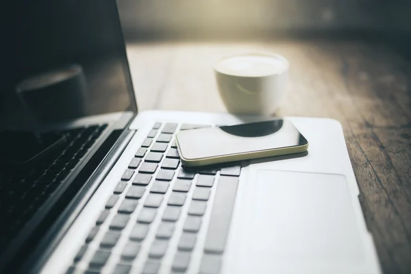 Mobiltelefon på laptop och fika på träbord — Stockfoto