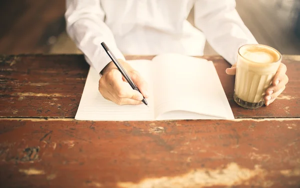 Man schrijven in Kladblok met kopje koffie in de linkerhand op houten — Stockfoto