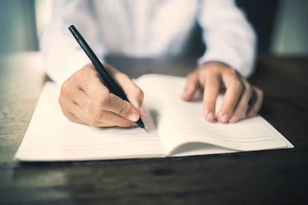 Girl writes in notebook on a wooden table — Stock Photo, Image