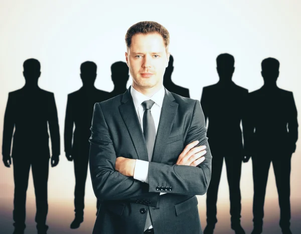 Leadership concept with handsome caucasian businessman in front of businesspeople silhouettes — Stock Photo, Image