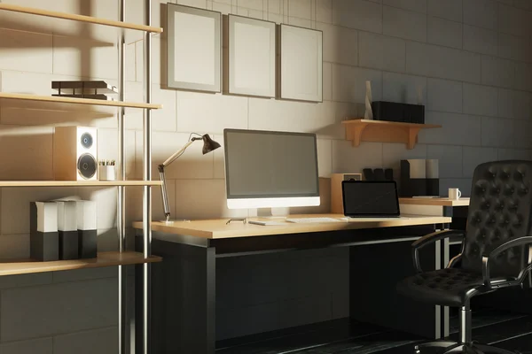 Vista laterale del luogo di lavoro creativo del progettista con monitor del computer vuoto, laptop, altoparlante, tazza di caffè e altri oggetti su sfondo muro di mattoni con tre cornici . — Foto Stock