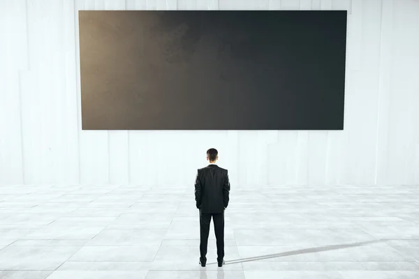 Geschäftsmann blickt auf schwarze Plakatwand — Stockfoto