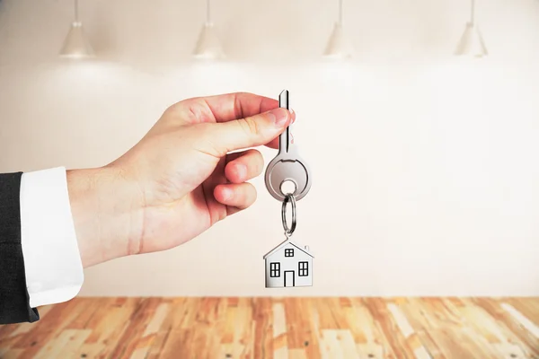Geschäftsmann mit Schlüsseln auf hellem, leeren Innenhintergrund. Immobilien- und Hypothekenkonzept — Stockfoto