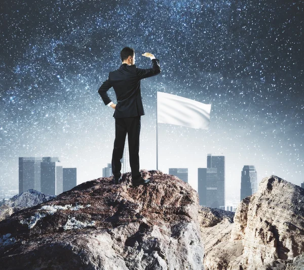 Leiderschap concept met zakenman op de bergtop met de witte vlag op zoek in de verte over stad achtergrond — Stockfoto