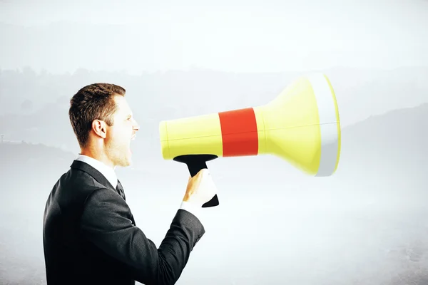 Vista lateral do empresário emotinal gritando em megafone em fundo cinza abstrato. Conceito de comunicação — Fotografia de Stock