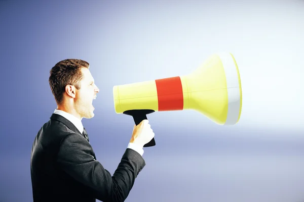 Side view of emotinal businessman screaming into megaphone on blue background. Communication concept — Stock Photo, Image