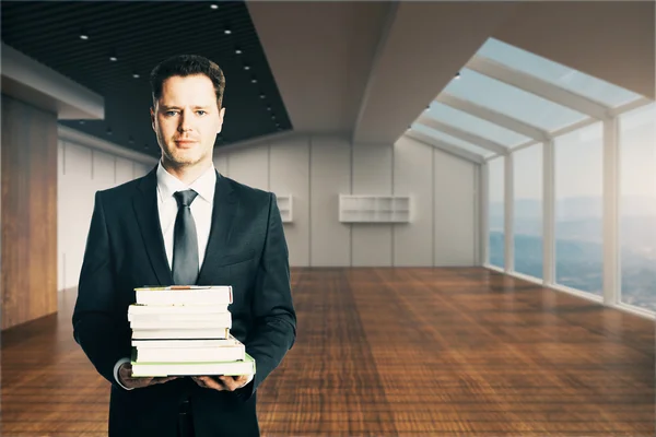 Handsome businessman holding stack of books in unfurnished modern interior. Education concept. 3D Rendering — Stock Photo, Image