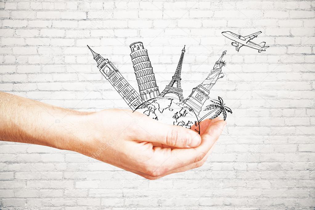 Man's hand holding abstract drawing of landmarks and airplane on white brick background. Traveling concept
