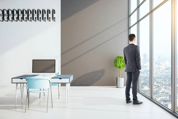Businessman standing in office room with computers and furniture. Occupation and worker concept.