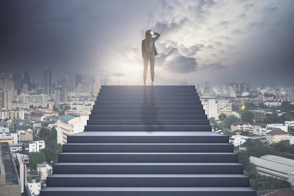 Businesswoman standing at the top of the concrete stairway thinking above the town, future success and growth concept