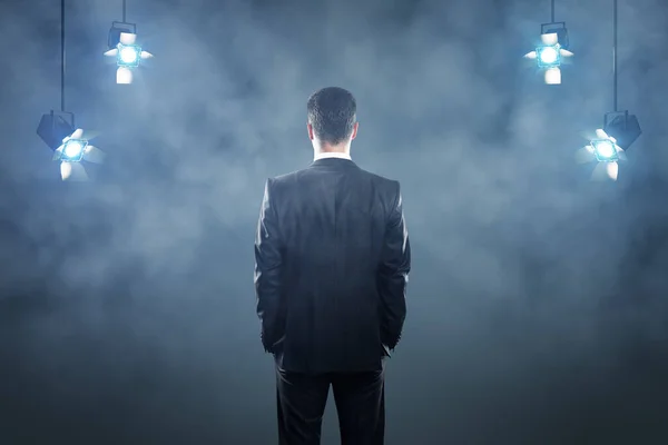 Leadership concept with businessman back on dark stage background with spotlights and smoke