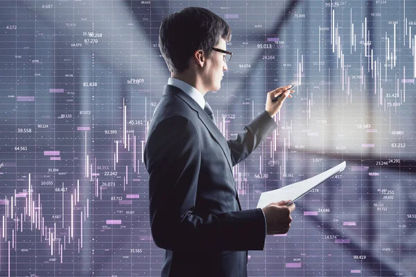 Businessman holding papers and touching a trading raising chart with a pen in an office corridor, stock market and trading concept