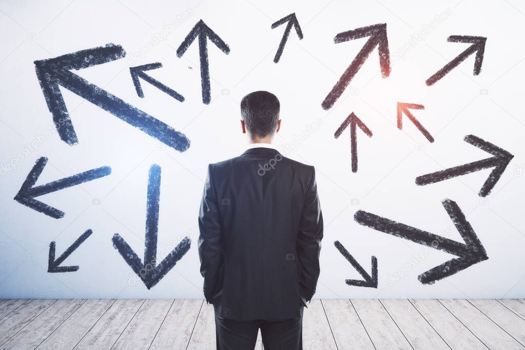Businessman standing puzzled in front of a wall with multiple black arrows pointed in different directions, decision making and career path concept