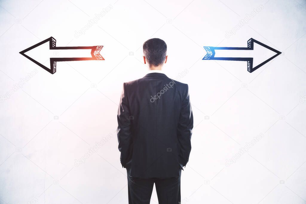 Businessman standing puzzled in front of a wall with two black silhouette arrows pointed in opposite directions, decision making and career pathway concept