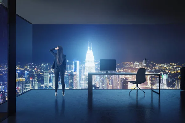 Back view of thoughtful young european businesswoman in modern glass office interior looking at illuminated night city. Success and tomorrow concept