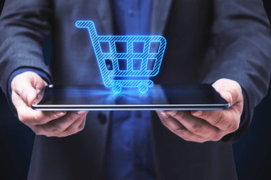 Mavi arka planda soyut alışveriş arabası bulunan tableti tutan işadamlarının yakınına. E-ticaret ve online alışveriş kavramı