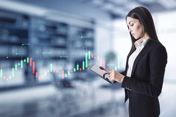 Attractive young european businesswoman with tablet using creative glowing forex chart interface in blurry office interior. Trade and invest concept. Double exposure