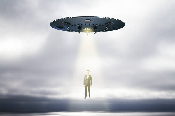 Abstract UFO with light taking businessman on sky background with mock up place. Spaceship, technology and mystery concept