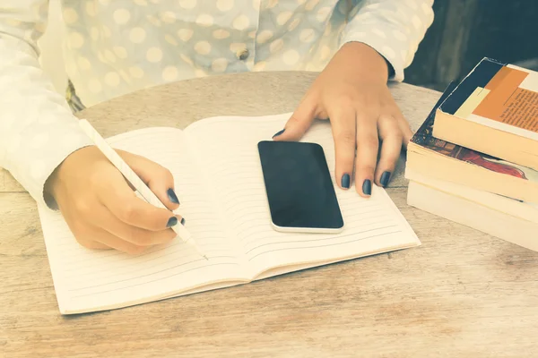 Fille écrit dans un carnet, avec téléphone portable — Photo