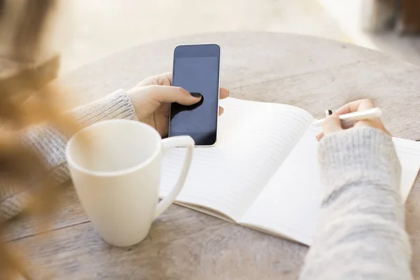 Fille écrit dans un carnet, avec téléphone portable — Photo