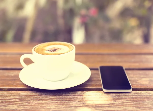 Telefon komórkowy i filiżankę kawy na drewnianym stołem — Zdjęcie stockowe