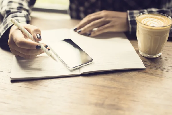 Meisje met mobiele telefoon dagboek en kop koffie in de houten tabl — Stockfoto