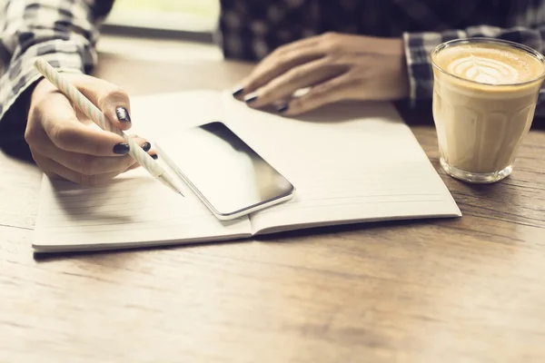 Ragazza con cellulare, diario e tazza di caffè al tavolo di legno — Foto Stock