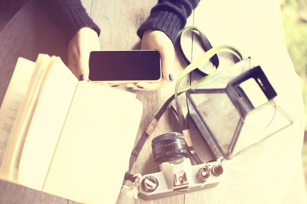 As mãos da menina com telefone celular, câmera velha e um livro em uma madeira — Fotografia de Stock