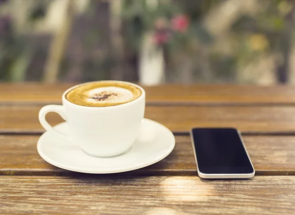 Cup of cappuccino and cell phone on a wooden table