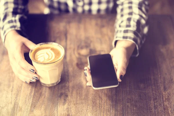 Hipster girl holding a coffee and cell phone on wooden table