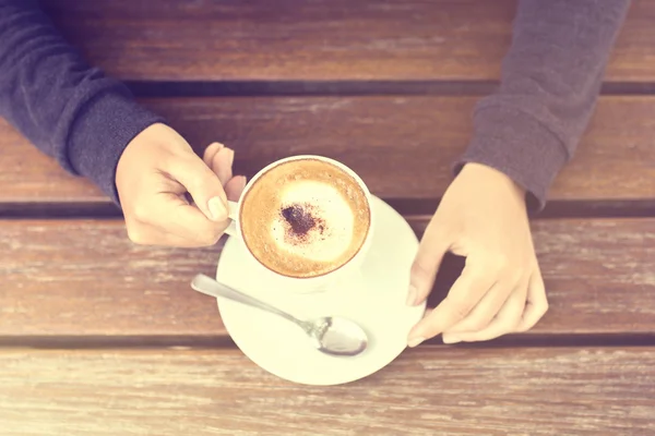 Κορίτσι που κατέχει ένα φλυτζάνι του cappuccino και ξύλινο τραπέζι — Φωτογραφία Αρχείου