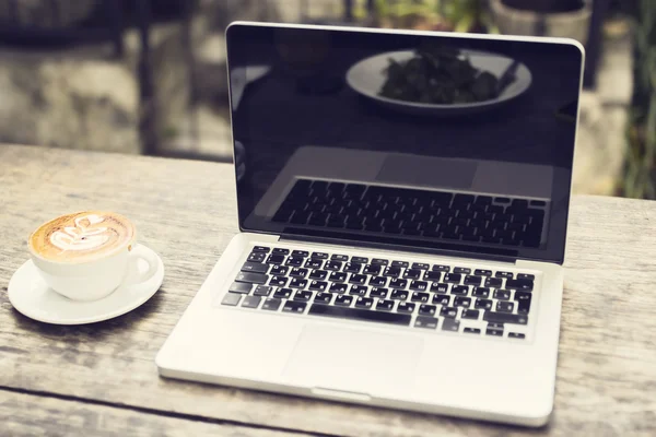 Laptop és egy fából készült asztal cappuccino csésze — Stock Fotó