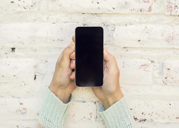 Jente som holder mobiltelefon og på en murvegg bakgrunn – stockfoto