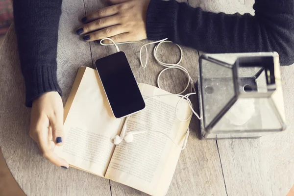 Mädchenhände mit Buch und Smartphone mit Kopfhörer — Stockfoto