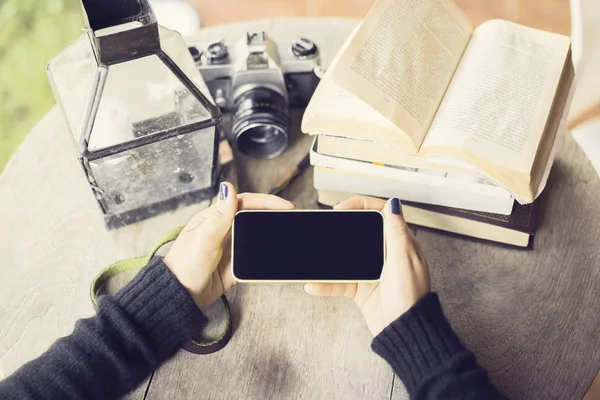 Fille mains avec smartphone, vieil appareil photo et livres sur un onglet en bois — Photo