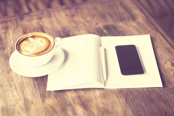 Diário em branco com xícara de café e smartphone em uma mesa de madeira , — Fotografia de Stock