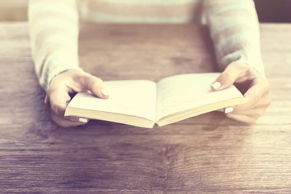 Flicka händer att hålla en öppen bok på ett träbord — Stockfoto